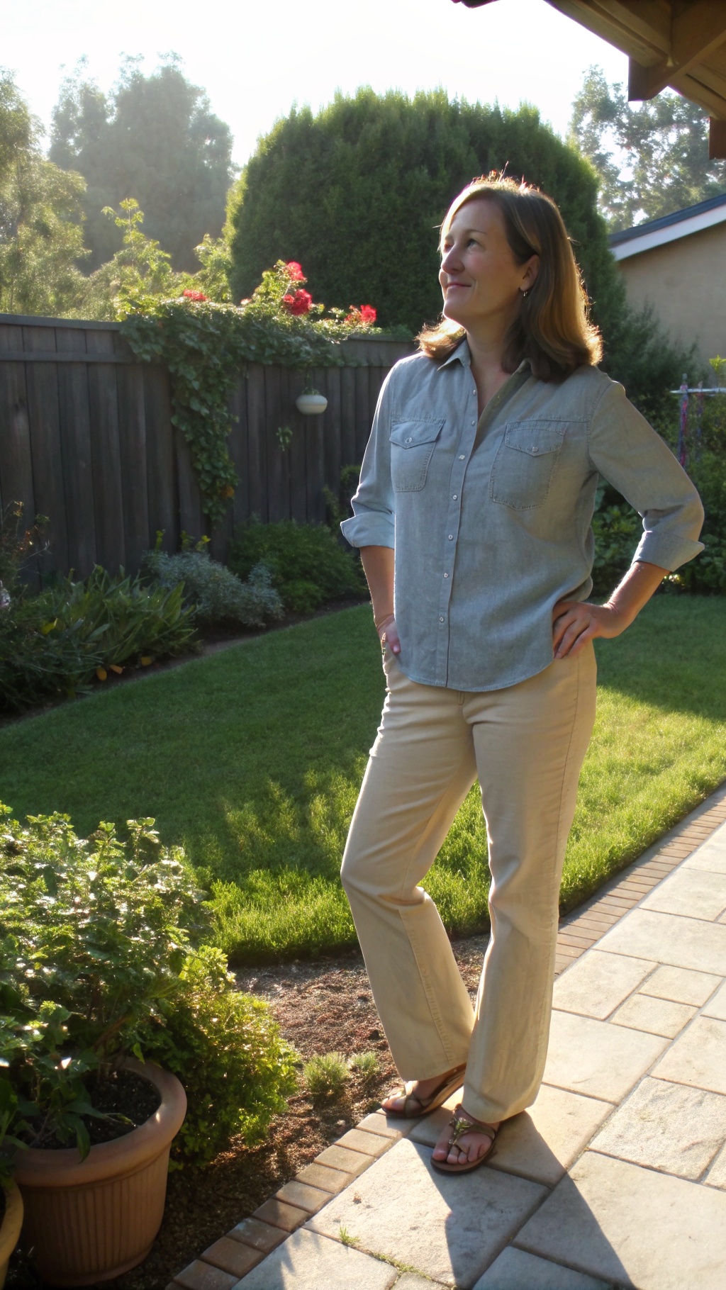 A woman wearing a lightweight chambray shirt and khaki pants, posing confidently in a garden.