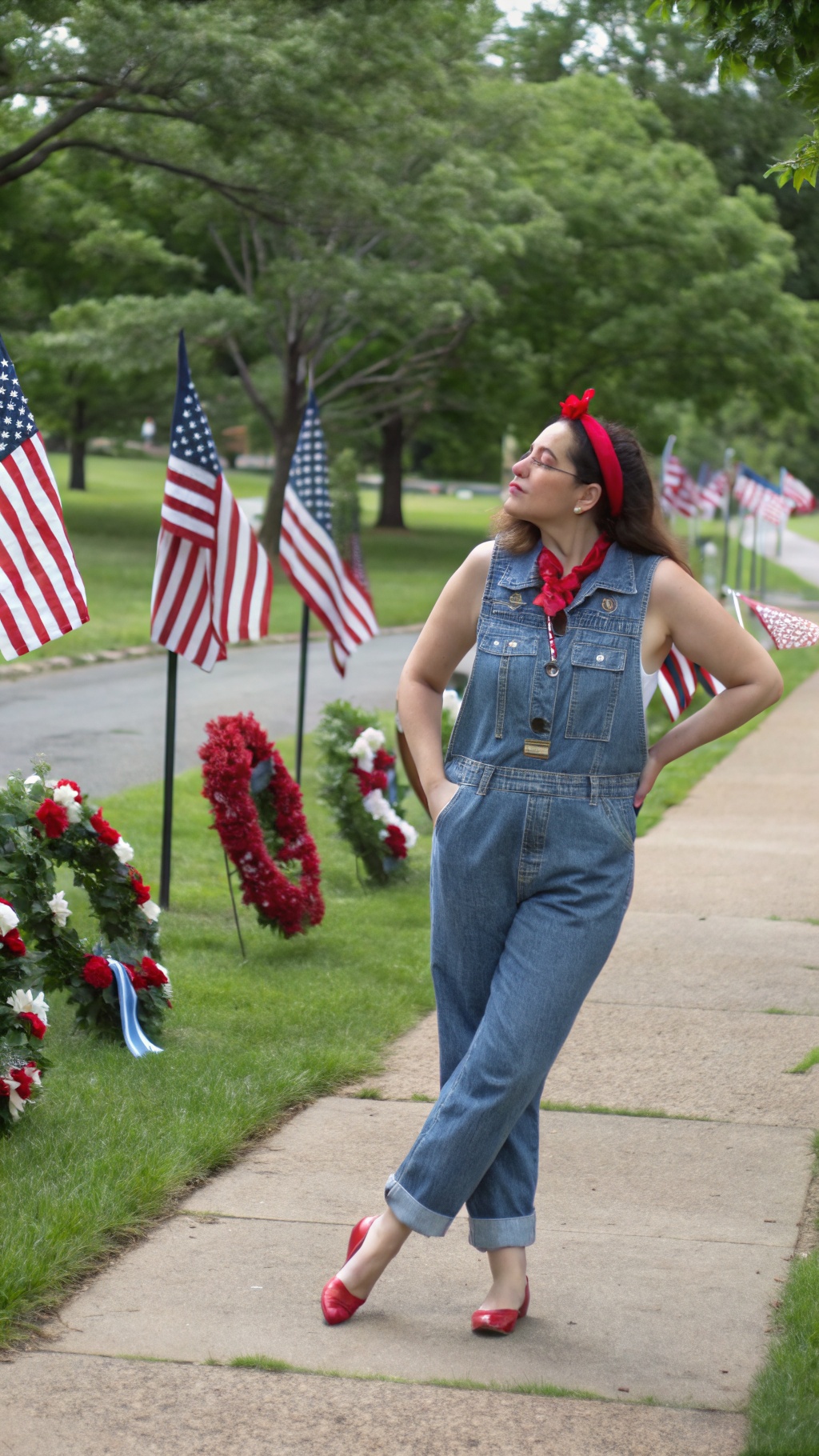 A woman in a denim jumpsuit with red accessories poses near American flags.