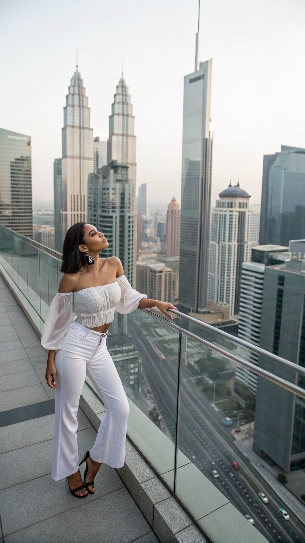 A woman posing in an off-the-shoulder top and white pants with a city view in the background