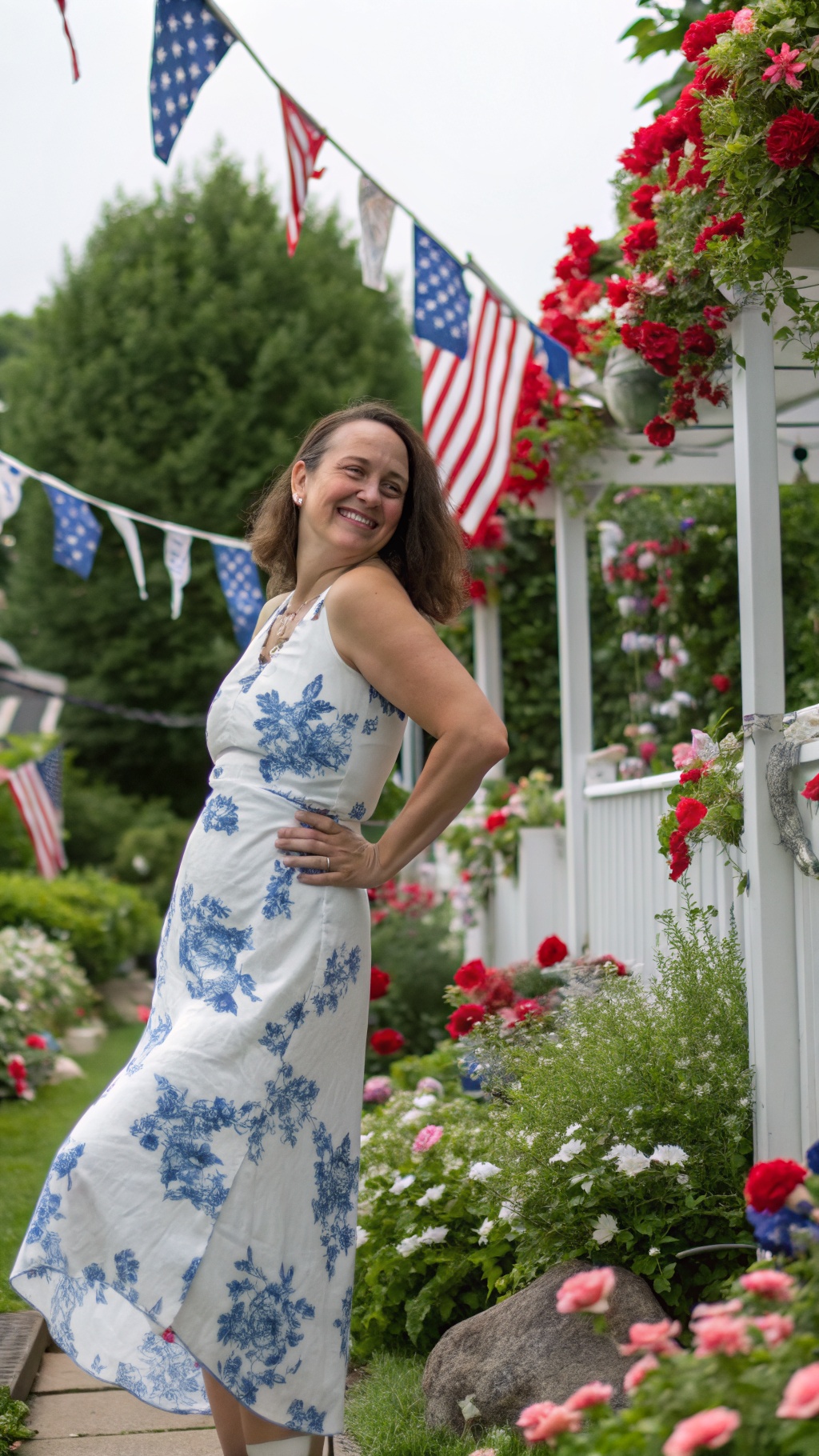 Woman posing in a white sundress with blue floral print surrounded by flowers and American flags.